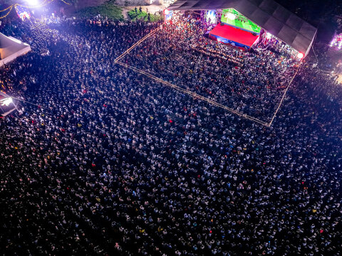 Dhaka, Bangladesh - 20 July 2026: Aerial view of a massive crowd gathered at an outdoor concert stage at night, with bright stage lights illuminating the audience.