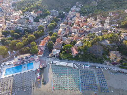 Aerial view of the coastal town of Sestri Levante featuring historic buildings, sandy beaches with rows of umbrellas, and a swimming pool by the sea in Sestri Levante, Liguria, Italy.