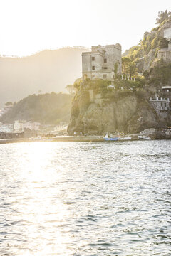 View of the historic Torre Aurora perched on a rocky cliff overlooking the sea at sunset in Monterosso al Mare, Liguria, Italy.