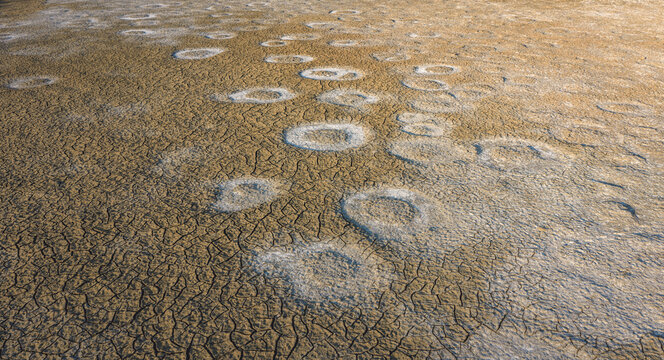 Aerial view of cracked dry earth with irregular white salt deposits forming an abstract textured pattern in France.