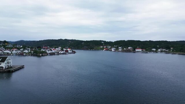 Aerial view of Grimstad harbor with small boats and coastal buildings under a cloudy sky in Grimstad, Agder, Norway.