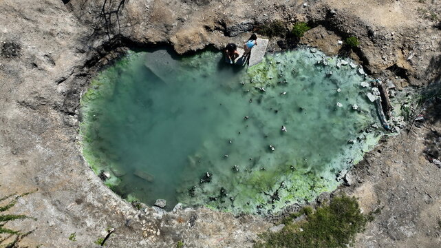 Aerial view of the DM Canoa thermal pool with turquoise water and people sitting on the rocky edge in La Canoa, Barahona, Dominican Republic.