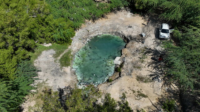 Aerial view of the natural pool at DM Canoa surrounded by lush green trees and dry terrain with a white vehicle parked nearby in La Canoa, Barahona, Dominican Republic.