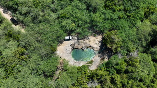 Aerial view of DM Canoa, a natural spring with clear turquoise water surrounded by dense green tropical vegetation and dirt paths in La Canoa, Barahona, Dominican Republic.