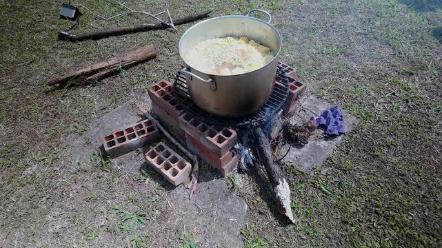 boiling a large pot of sancocho de gallina (colombian chicken soup) on an outdoor wood fire pit
