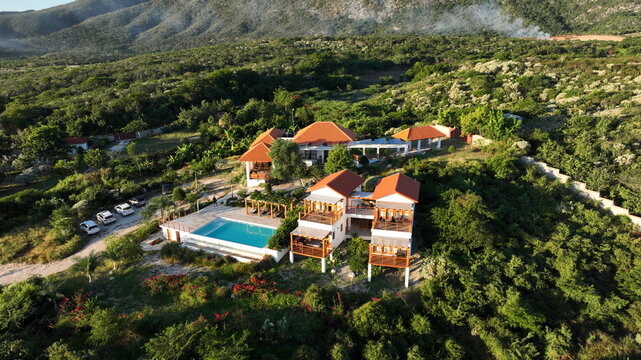 Aerial view of Altos de La Caobita Eco-hotel featuring a swimming pool and wooden structures surrounded by lush tropical vegetation and mountains in Barrera, Azua, Dominican Republic.