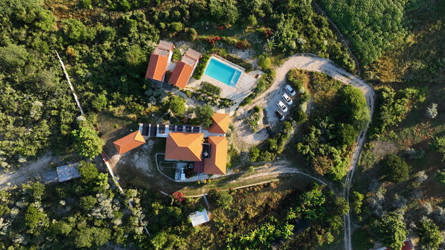 Aerial view of Altos de La Caobita Eco-hotel featuring terracotta-roofed buildings, a swimming pool, and surrounding lush vegetation in a rural landscape in Barrera, Azua, Dominican Republic.