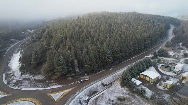 Aerial view of a road winding through a snowy forest near a small industrial area in Coyhaique, Aysen, Chile.