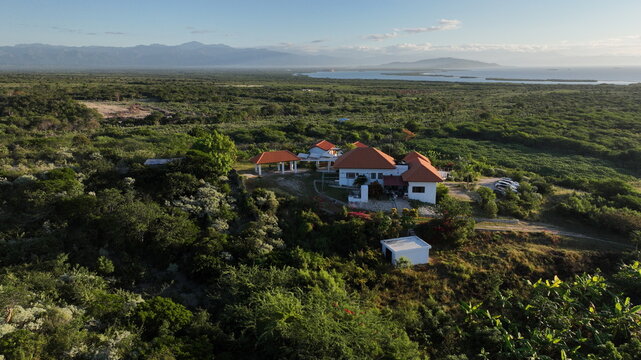 Aerial view of Altos de La Caobita Eco-hotel surrounded by lush green vegetation, trees, and coastal landscape near the sea in Barrera, Azua, Dominican Republic.