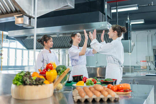 Cooking teacher and student girls smiling and high fiving during culinary class, Happy kids and culinary instructor celebrating success with high five gesture in commercial cooking school kitchen