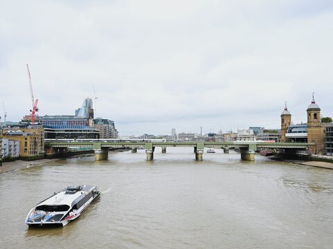 View of the Cannon Street Railway Bridge spanning the River Thames with a river bus passing underneath and the London skyline in the background in London, England, United Kingdom.
