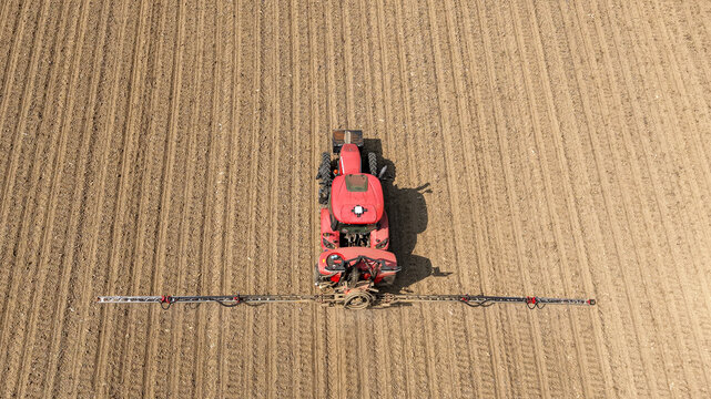 Aerial view of a red tractor applying herbicide across a cultivated farm field in Mediglia, Lombardy, Italy.