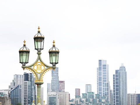 View of an ornate Victorian lamp post with a golden emblem against the modern skyline of London, England, United Kingdom.