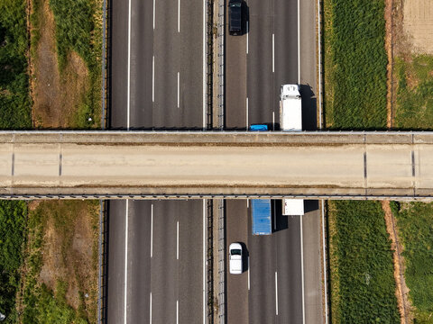Aerial view of traffic moving along a highway with cars and trucks passing under a bridge in Milan, Lombardy, Italy.