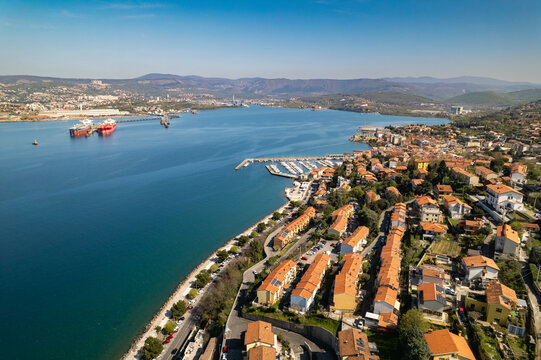 Aerial view of the coastal town of Muggia with its terracotta-roofed houses, marina, and the blue waters of the Gulf of Trieste in Trieste, Friuli-Venezia Giulia, Italy.
