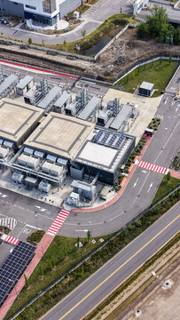 Aerial view of a modern data center facility featuring industrial cooling units, solar panels on the roof, and secure perimeter roads, Settala, Lombardy, Italy.
