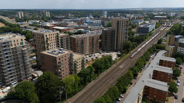 Stevenage, England, United Kingdom - 16 July 2026: Aerial view of modern residential apartment buildings situated next to a railway line with a train passing through the urban landscape.