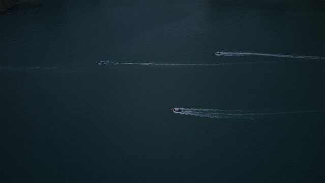 Aerial view of three small boats leaving white wakes as they travel across the dark water of the Andaman Sea in Ao Nang, Krabi, Thailand.