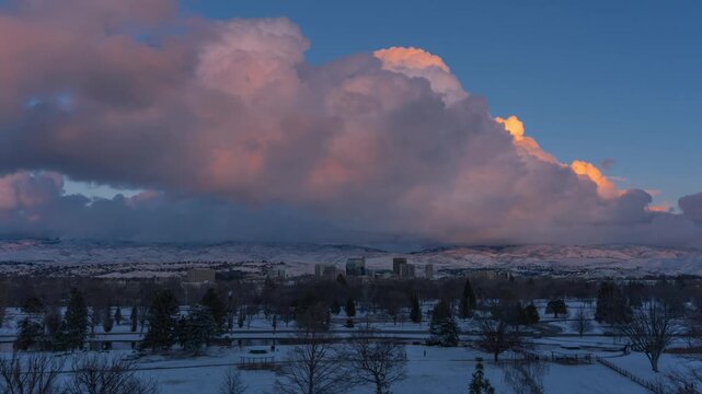 Aerial view of Ann Morrison Park with snow-covered grounds and trees under dramatic sunset clouds over the Boise city skyline in Boise, Idaho, United States.