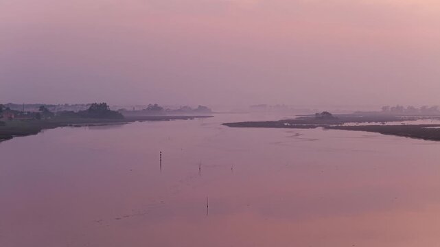 Aerial view of Aveiro Lagoon at sunset with calm waters reflecting the pink sky and surrounding marshlands in Aveiro District, Portugal.