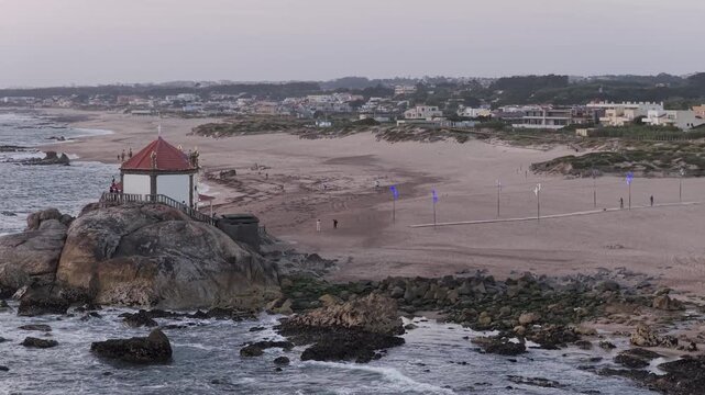 Aerial view of the historic Senhor da Pedra chapel perched on a rocky outcrop above the sandy coastline in Vila Nova de Gaia, Porto, Portugal.