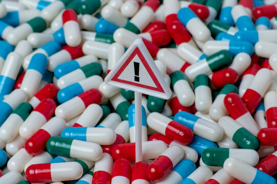 Warning sign standing in a dense pile of colorful capsule pills. Medication risk and side effects, drug overdose concept.