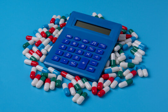 Blue calculator and a pile of colorful medical capsules against a blue background. Healthcare costs, medical insurance budgeting, pharmaceutical expenses concept.