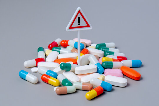 Warning sign standing in a dense pile of colorful capsule pills. Medication risk and side effects, drug overdose concept.