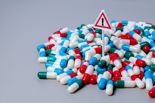 Warning sign standing in a dense pile of colorful capsule pills. Medication risk and side effects, drug overdose concept.