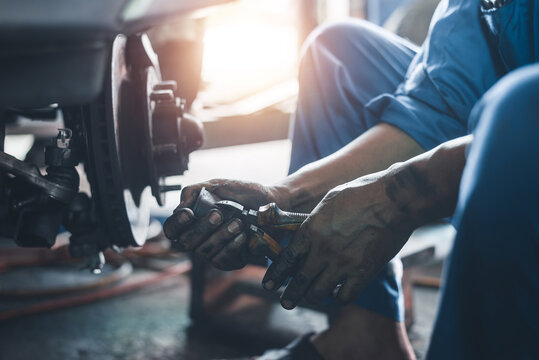 Auto mechanic working on old vehicle brake and suspension system with hand tools in garage, authentic photo, not AI.