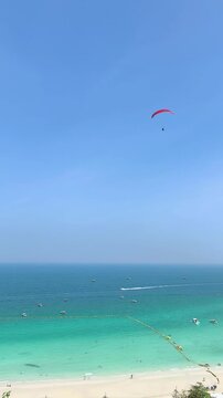 Aerial view of a red parasail flying high in the clear blue sky over a beautiful tropical beach and turquoise ocean.