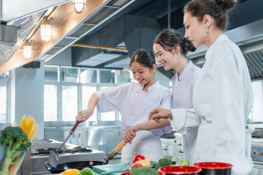 Female chef teacher guiding young students cooking in commercial kitchen, Culinary instructor helping kids with cooking class in restaurant kitchen