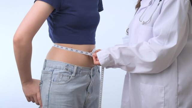 Determined female patient receives waist measure from professional doctor at clinic starting healthy weight loss journey with tape