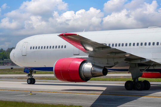 Large white passenger plane with red engine cowlings moves slowly across the tarmac on a sunny day at the airport to prepare for takeoff
