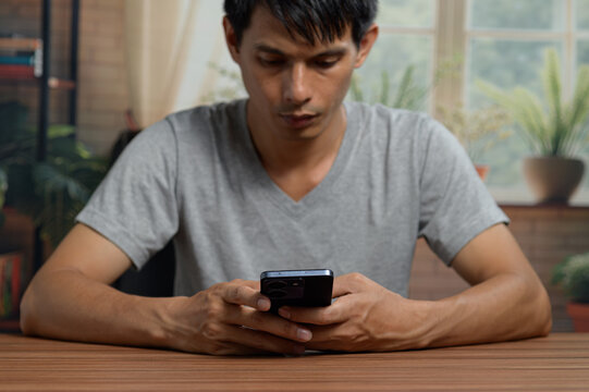 Young Man Using Smartphone at Wooden Table in Bright Indoor Setting