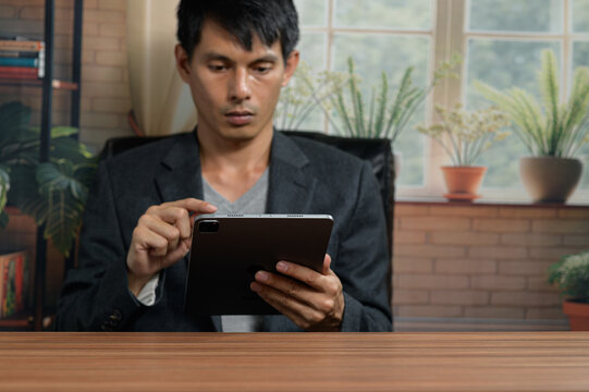 Man Using a Tablet at a Desk in a Bright, Home Office with Plants