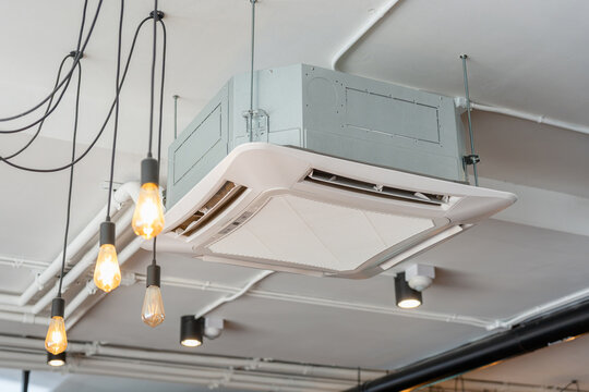 Modern cassette type air conditioner installed on ceiling with vintage hanging lamps, Industrial style ceiling mounted air conditioner unit in modern office or cafe