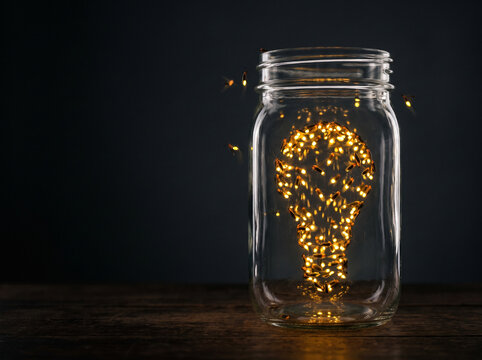 Glass jar of fireflies gathered into the shape of a light bulb