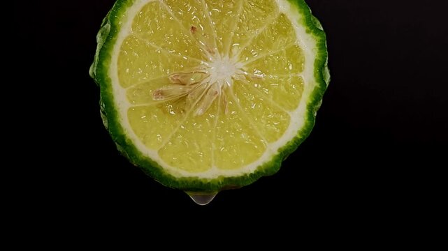 Sliced kaffir lime on black background with water drop.