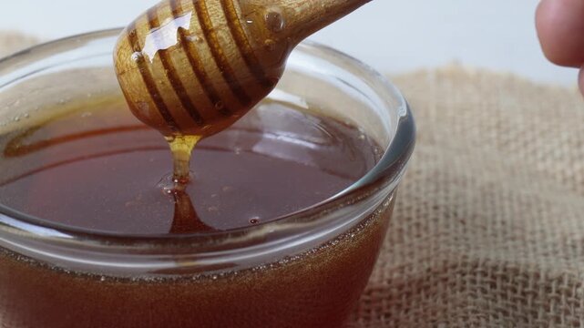 Honey dripping in the glass jar from honey dipper 