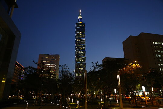Taipei 101 skyscraper towers above city street lights at night.