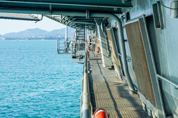 Outer Passageway Gangway Deck on Military Warship at Sea. Perspective view along the metal gangway deck railing of a naval warship, overlooking clear blue ocean waters, distant coastline and mountain. © joeyphoto