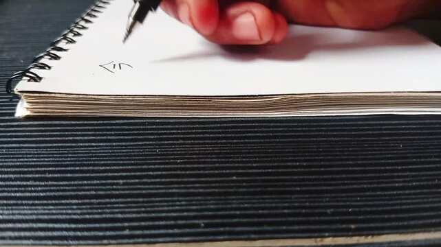 Close up of hand writing Japanese kanji characters with black pen on blank notebook, education and language learning concept.
