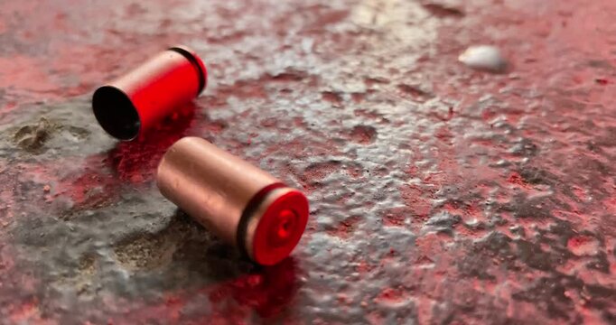 Spent cartridge cases lie on the ground reflecting red and blue emergency lights from a police vehicle.