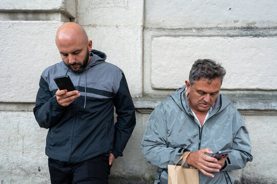 Men browsing smartphones focusing on screen against wall