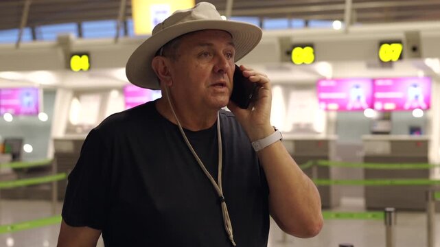Mature male traveler talking on the phone at the airport check-in counter