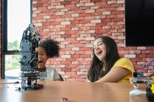 Cheerful children exploring robotics and engineering in classroom, Happy multiethnic schoolgirls laughing while learning robotics and coding in STEM class