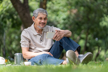 Obraz premium elderly pensioner man spend leisure time relaxing in urban park,sitting and surfing internet on smartphone