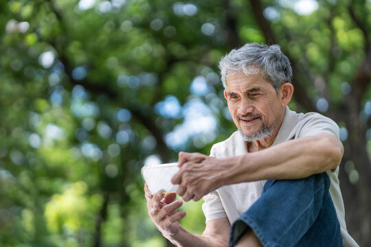 elderly pensioner man spend leisure time relaxing in urban park,sitting and surfing internet on smartphone