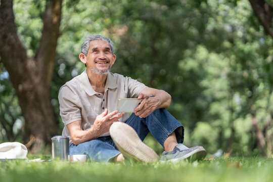 portrait elderly pensioner man spend leisure time relaxing in urban park,sitting,using smartphone,looking away and smiling
